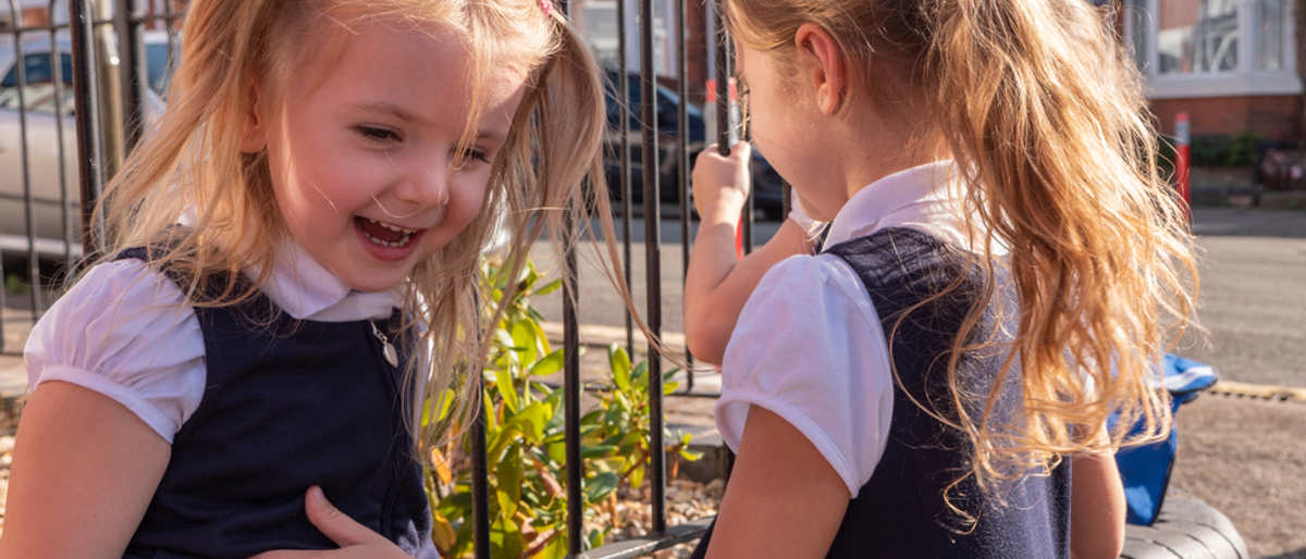 Two young primary school girls laughing together in the playground.
