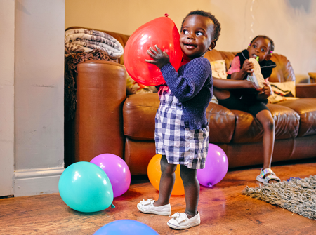 Child smiling holding a balloon in a living room.