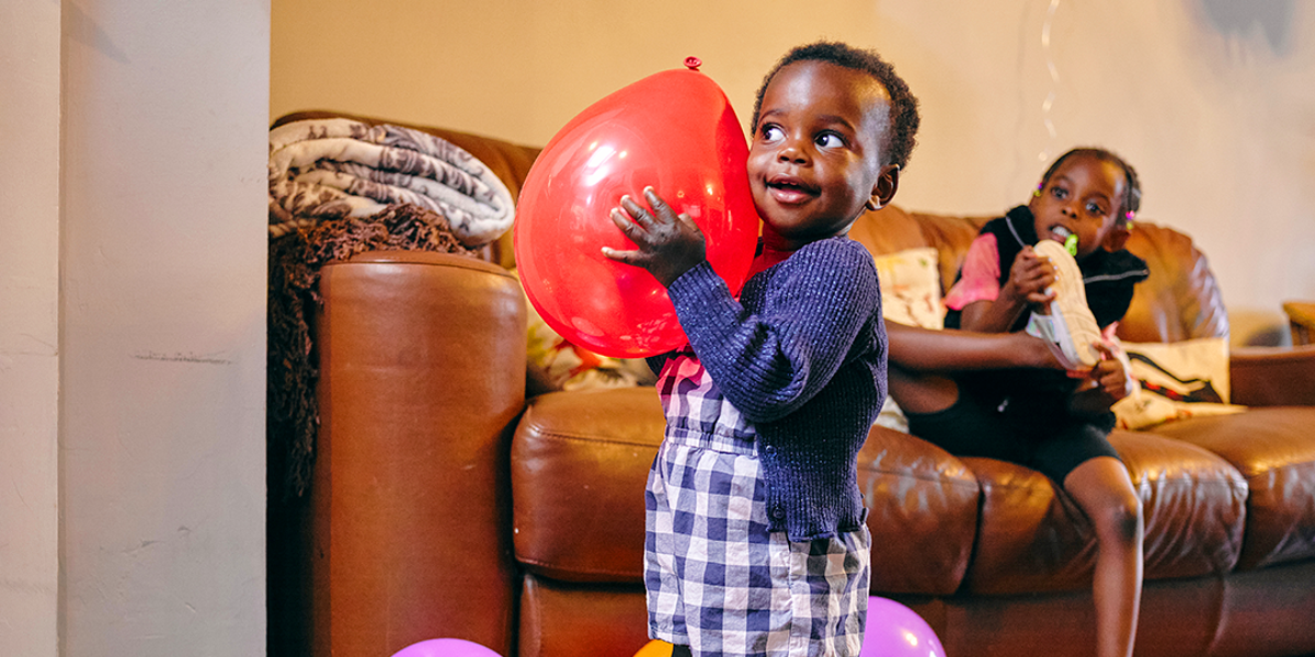 Child smiling holding a balloon in a living room.