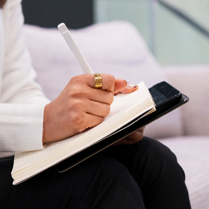 Woman writing on a notepad on top of a tablet