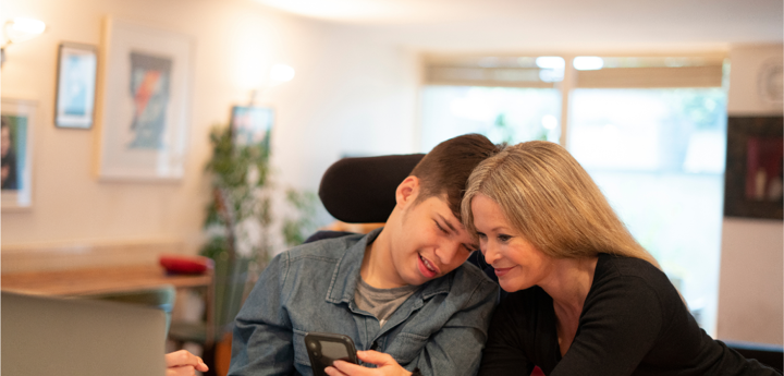 Disabled Young Adult Looking At Phone With Adult