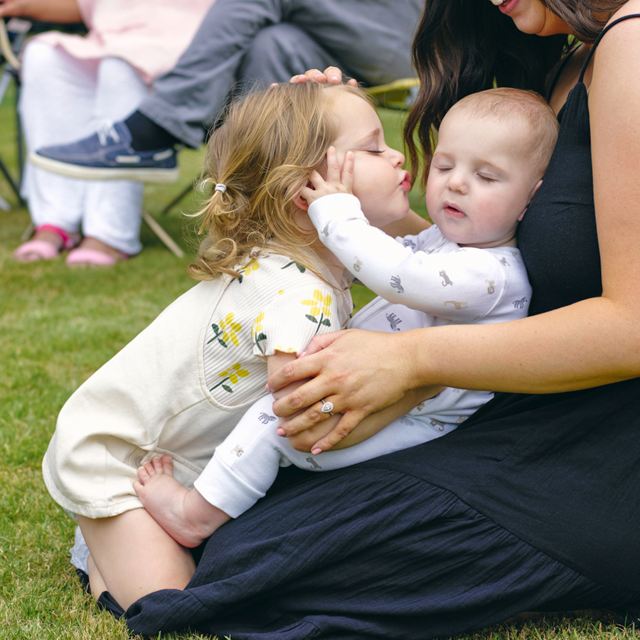 Child Kissing Baby On Adult Womans Lap