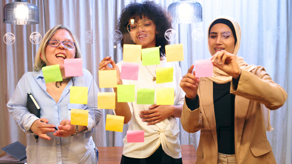 3 smiling women putting Post-It notes on a glass screen