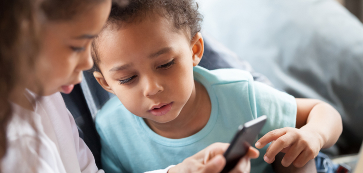 Young girl on mobile phone with a younger boy peering over her shoulder to look at the mobile phone.