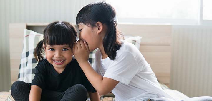 girl whispering into ear of laughing friend