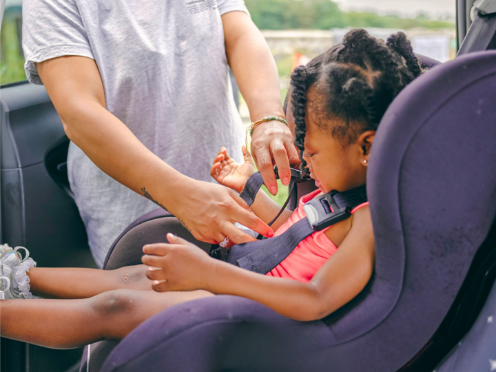 Child Being Clipped Into A Car Seat By Adult