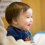 Smiling baby sitting down wearing a blue jumper.