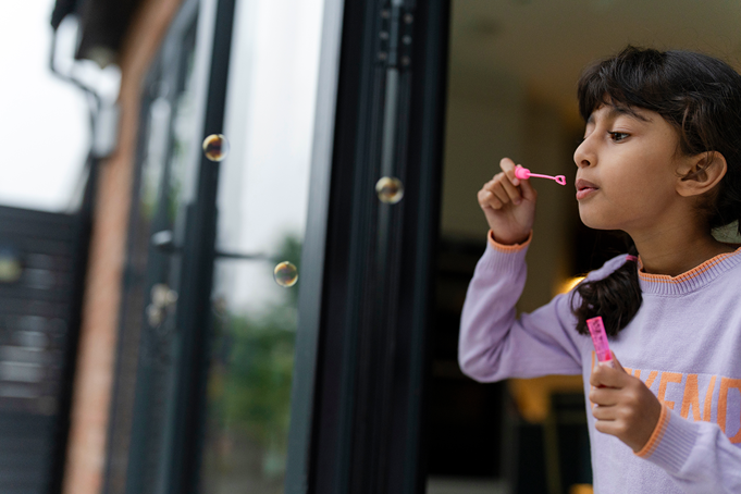 girl in a doorway blowing bubbles into a garden