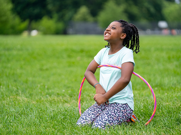 Young girl sitting in the middle of a grass field with a hula hoop around her.