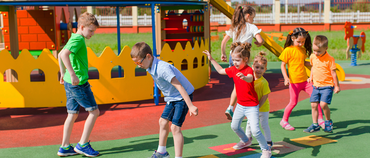 7 children playing hopscotch in playground.