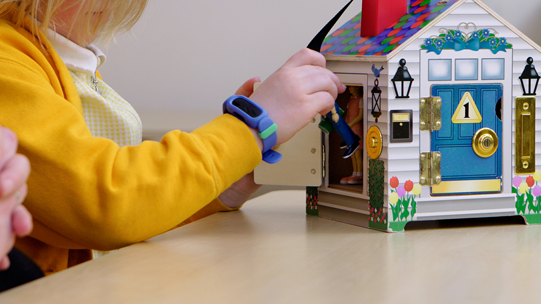 Child in yellow cardigan playing with a toy house